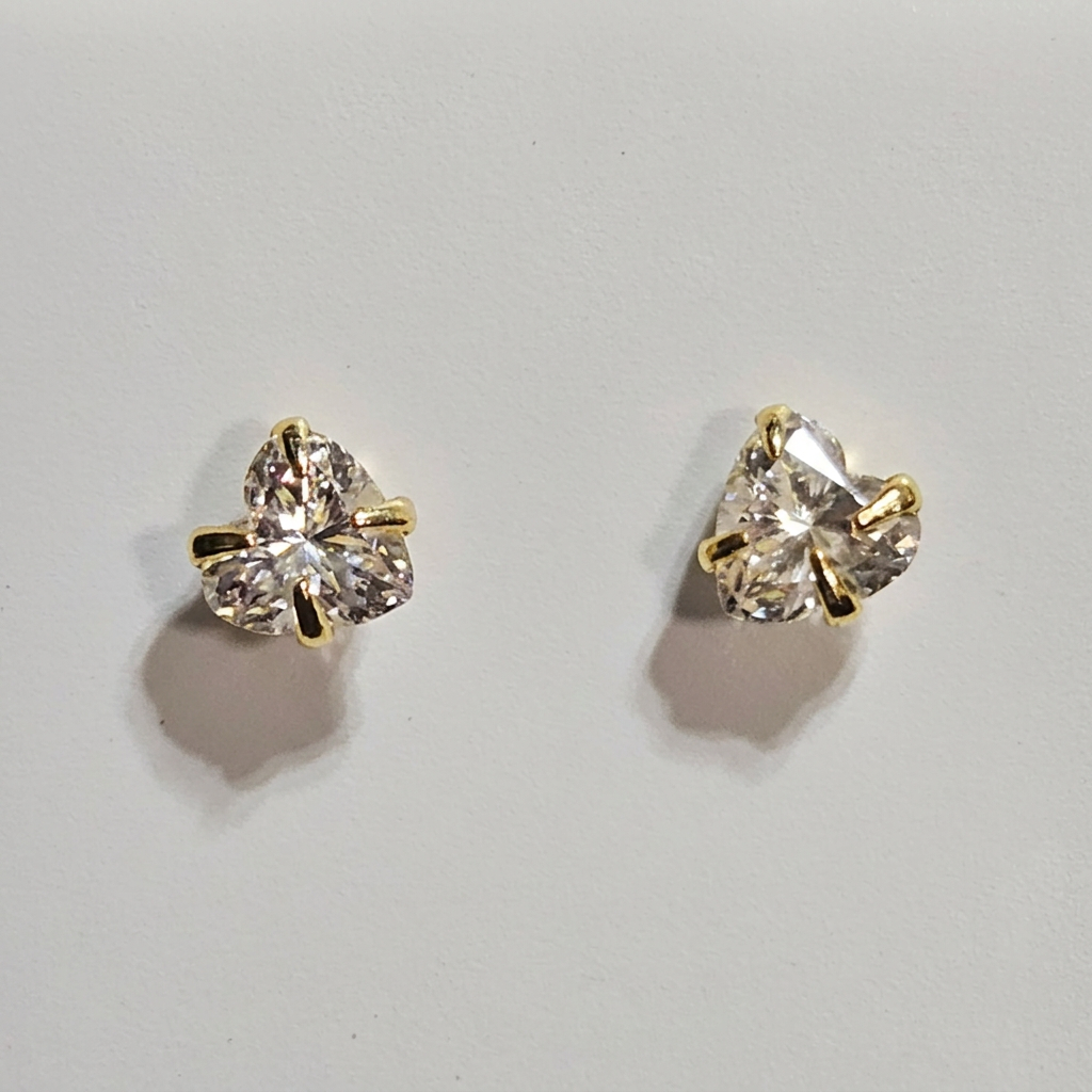 Close-up of heart-shaped clear stone stud earrings with gold-tone prongs